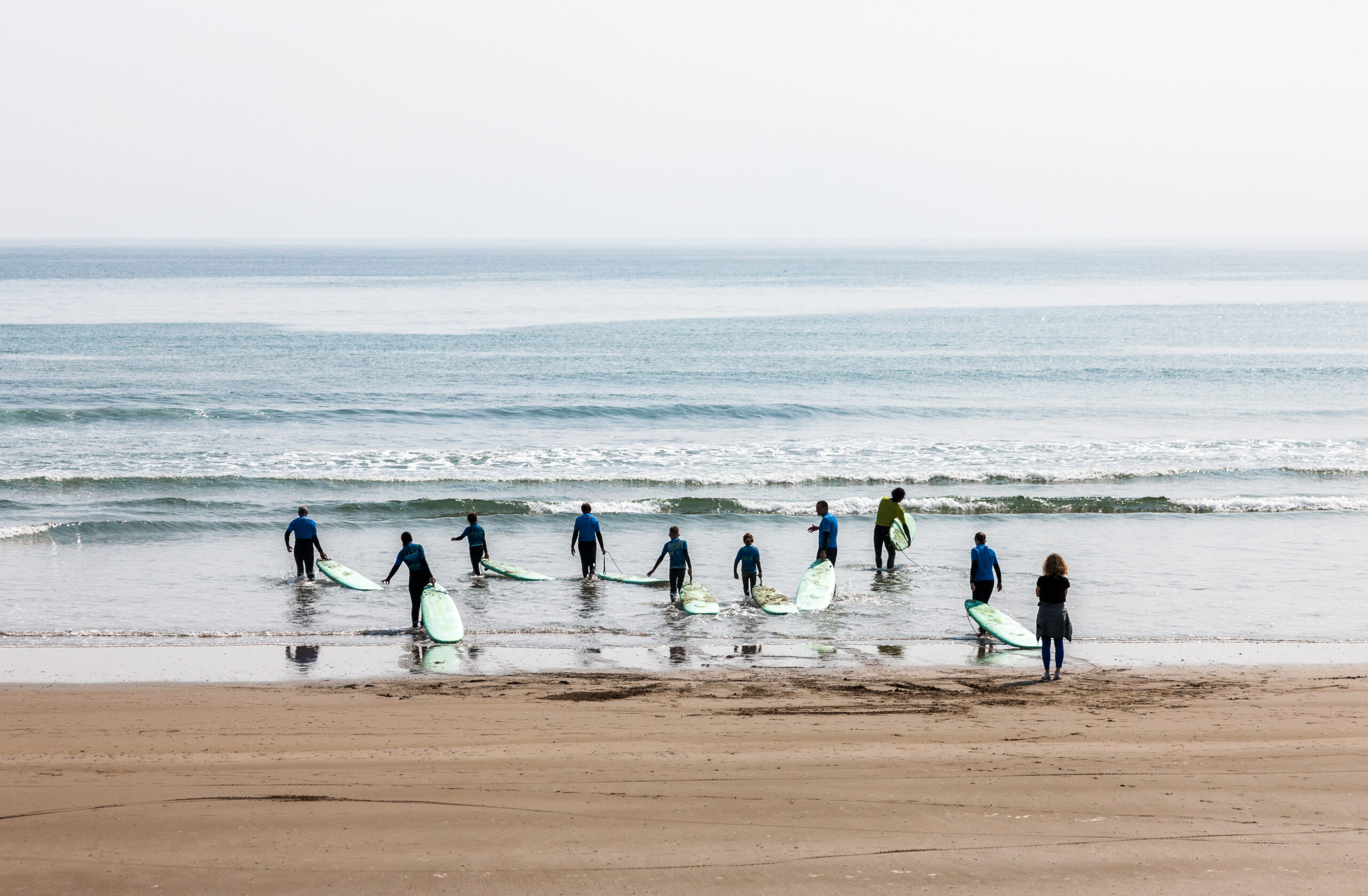 10 young people walking towards the coastline with surfboards at Garretstown Beach, County Cork.