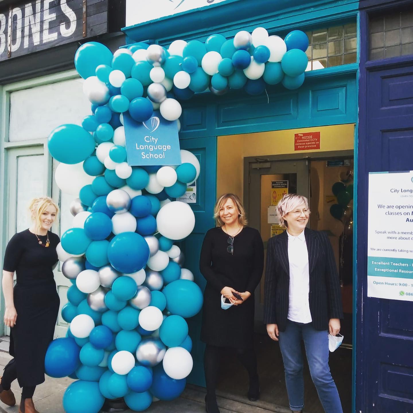 teachers smiling standing outside city language school with a blue and white balloon arch over the door