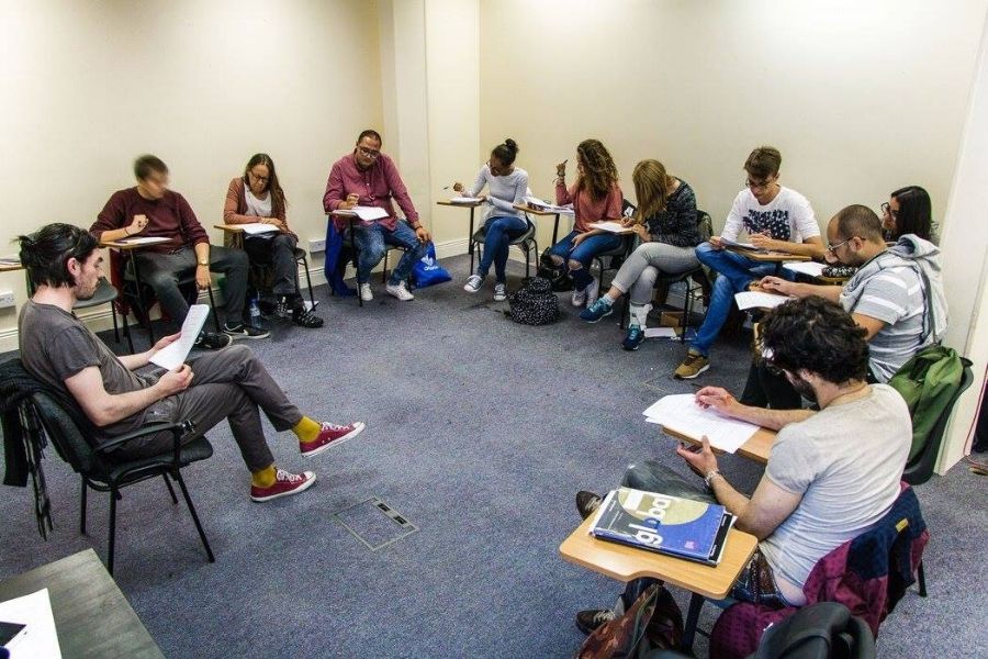 teacher addresses a group of english language students sitting at desks in a circle