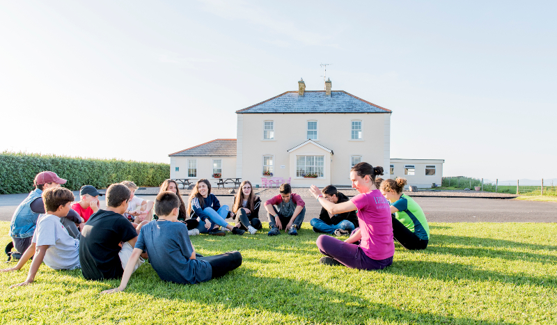 a group of junior students sitting having english class on the grass outside donegal english language school dels