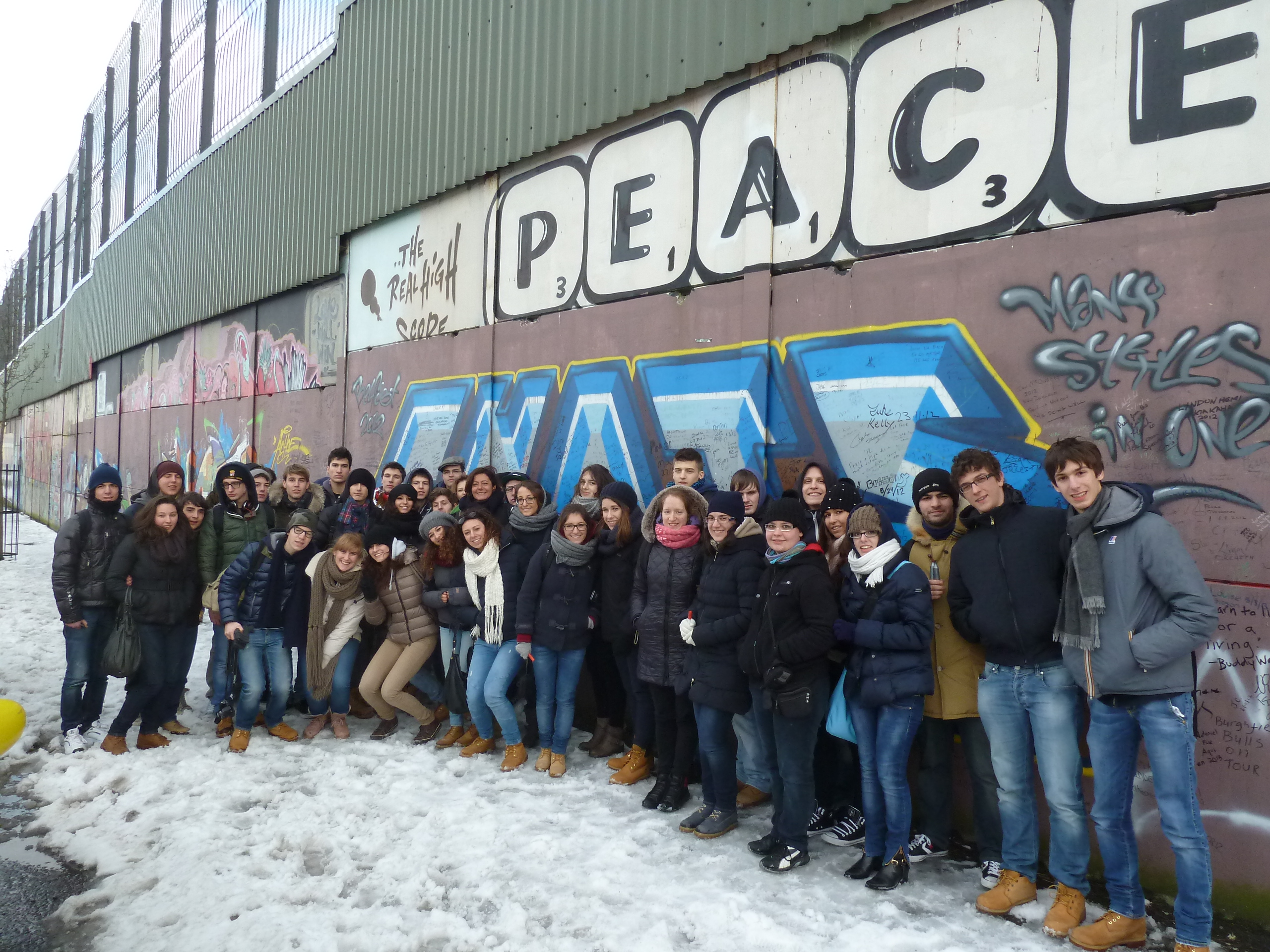 big group of students smile and pose in front of peace wall