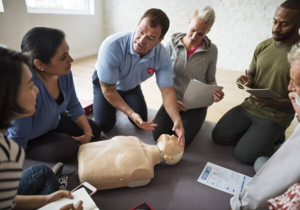 A first aid training session. One person instructs the group on a dummy.